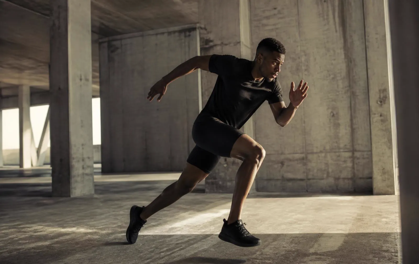 Male athlete accelerating in explosive movement across a concrete hall